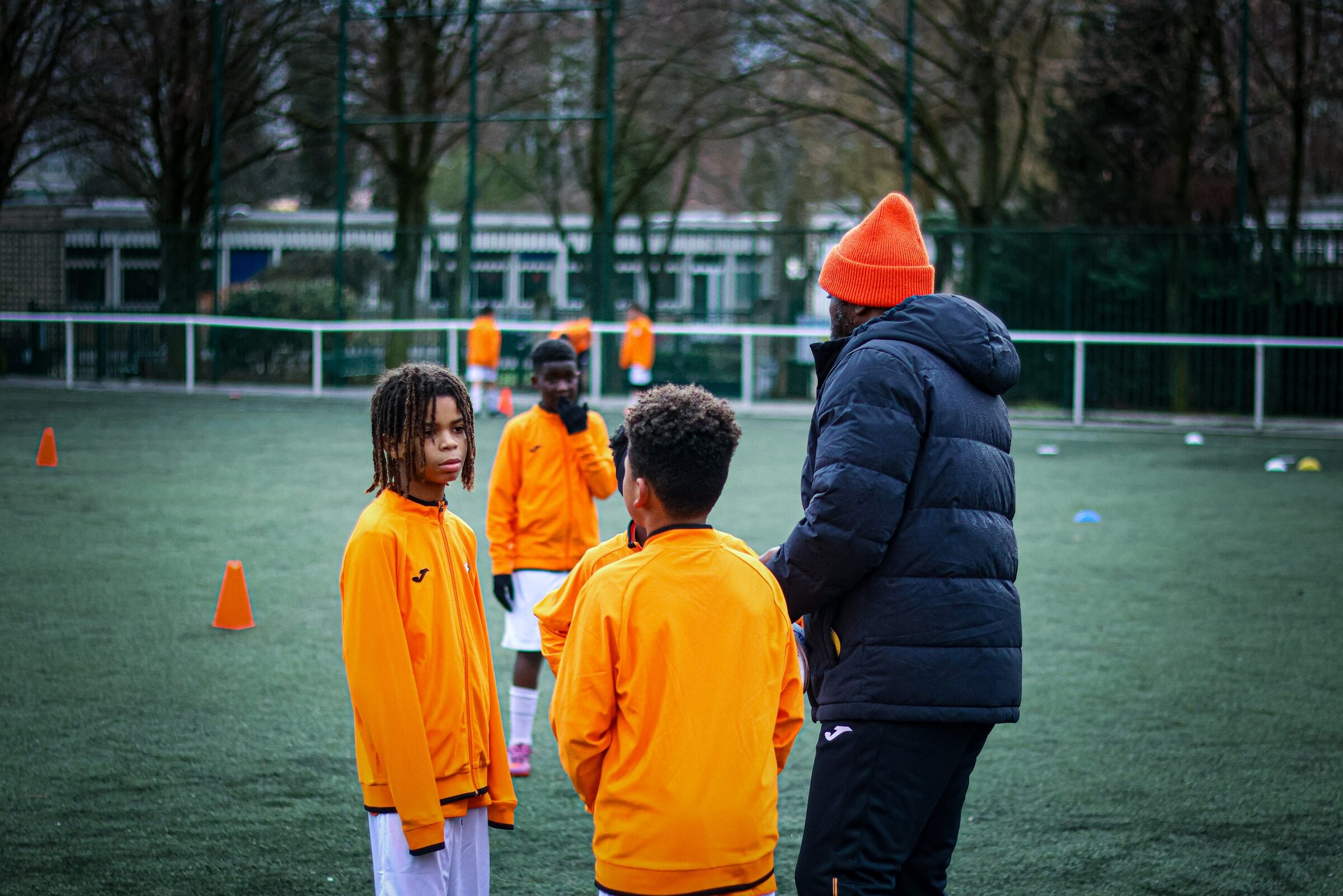 Un éducateur AB Football Académie échange avec deux jeunes joueurs sur le terrain