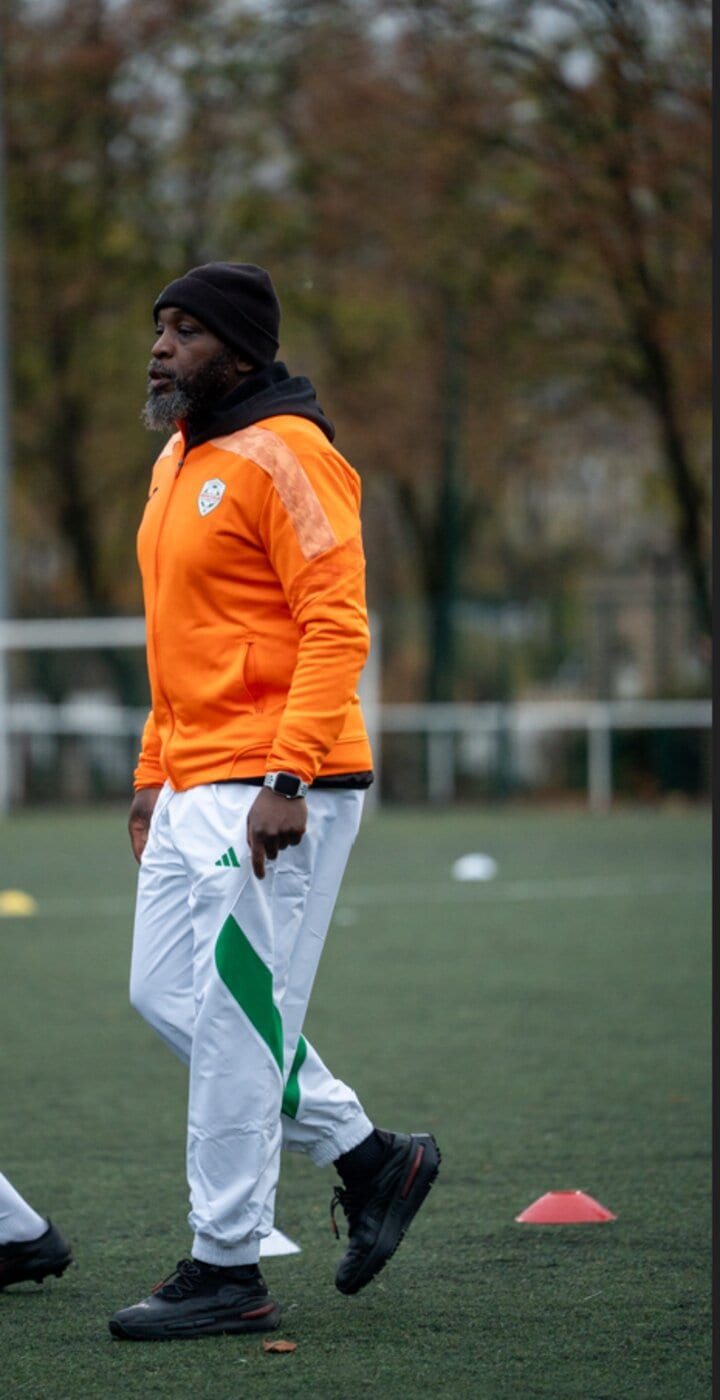 Portrait du coach principal AB Football Académie, veste orange, sur le terrain